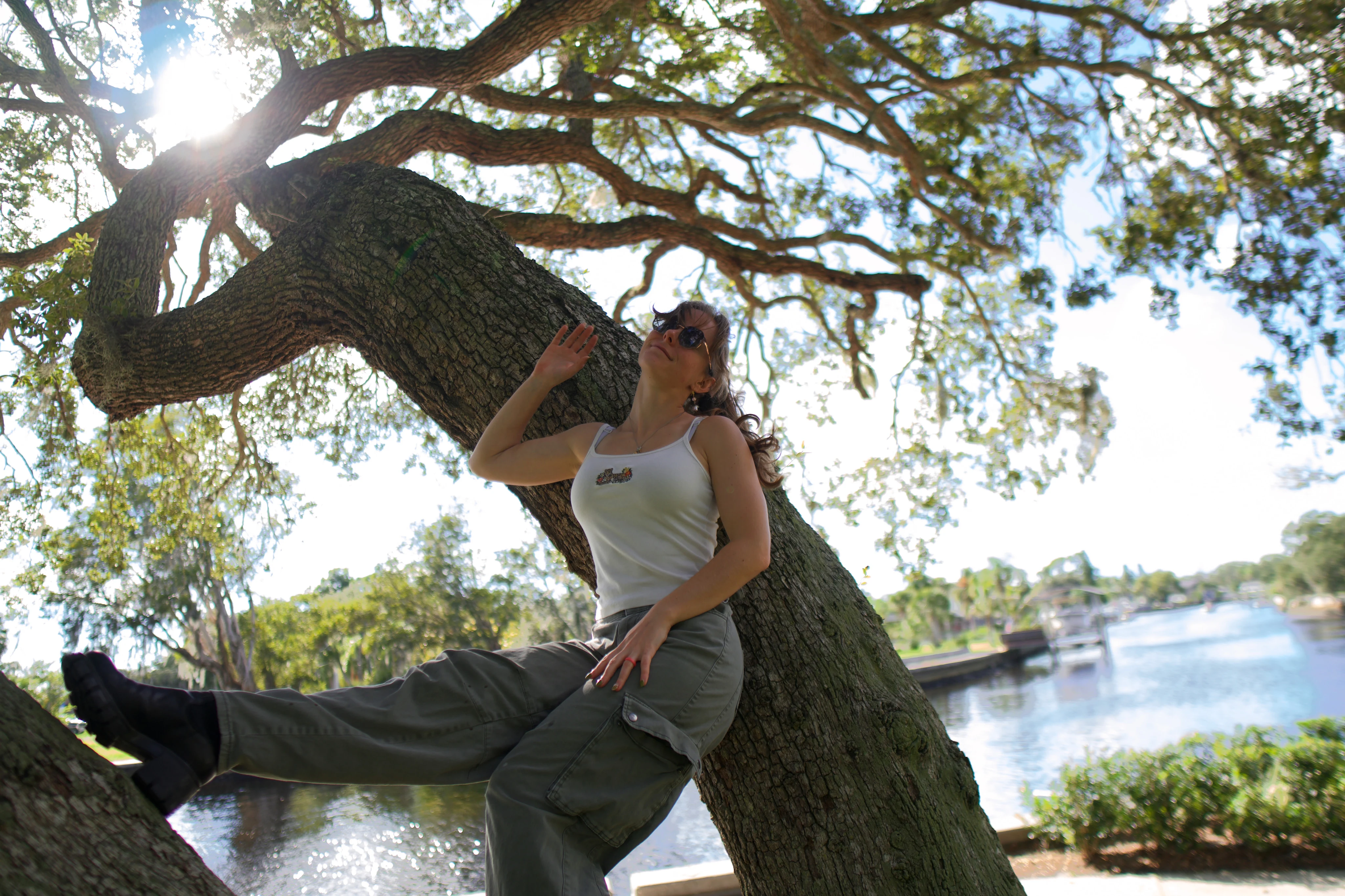 A woman seated on an oak trunk with a hand raised to the branch above her