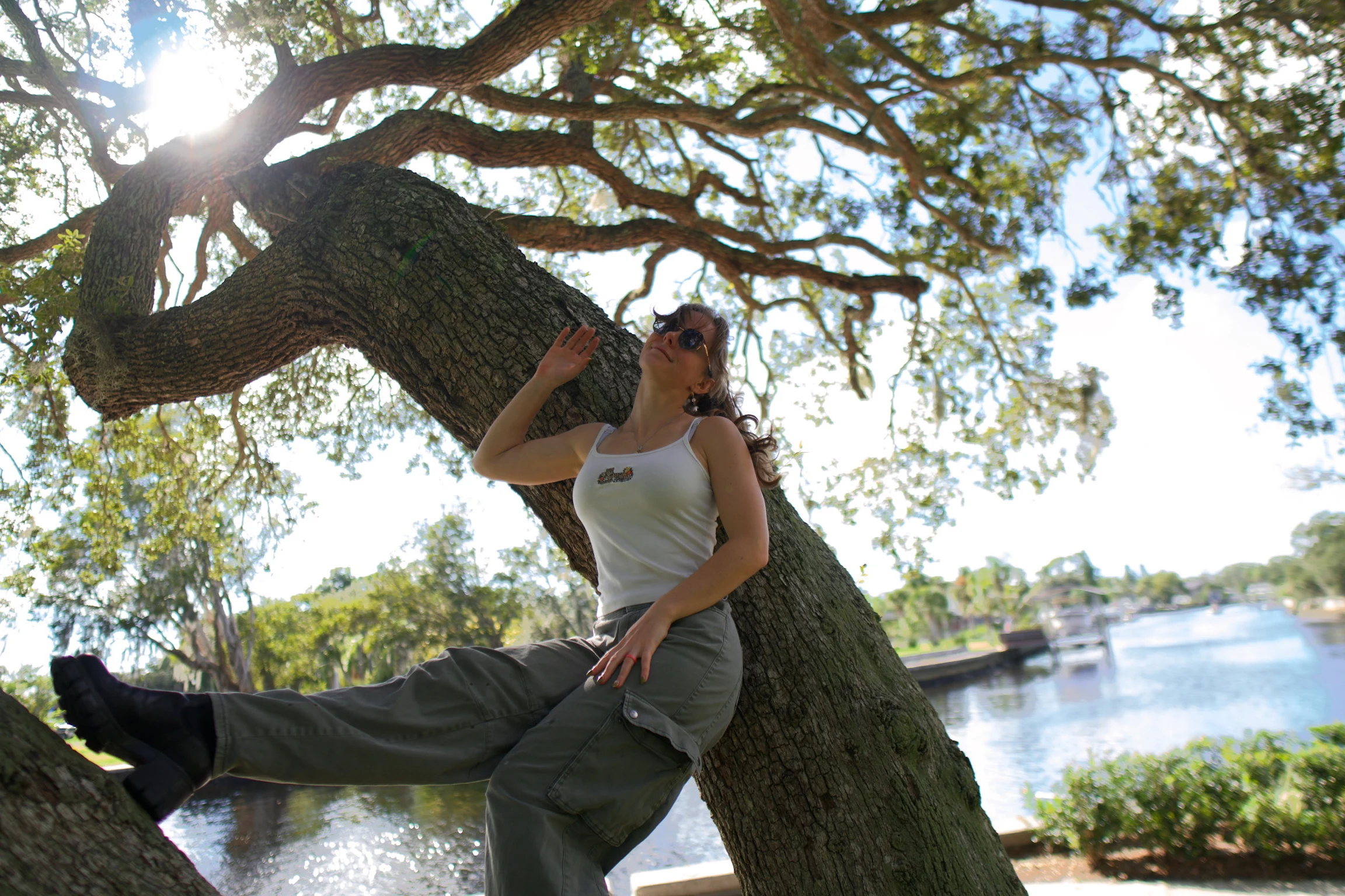 A woman seated on an oak trunk with a hand raised to the branch above her