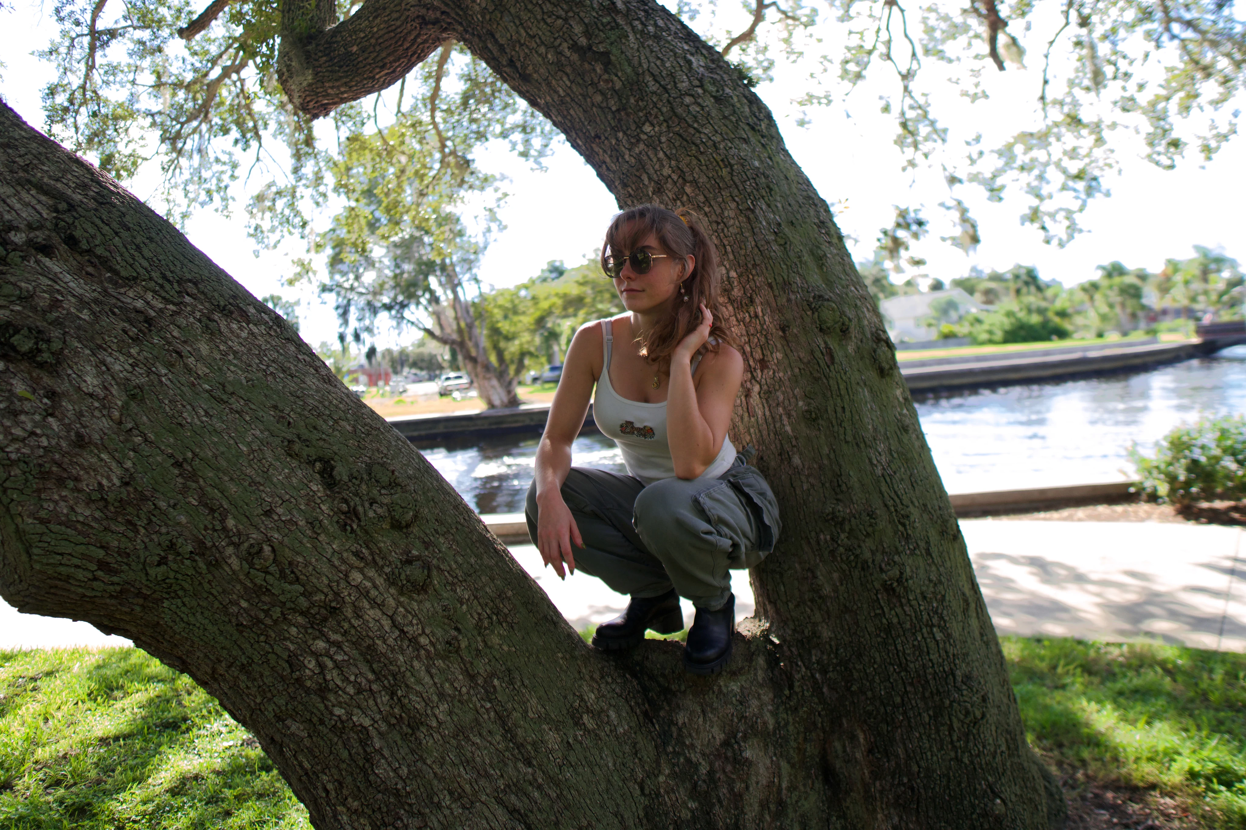 A woman crouched at the base of an oak, looking at the camera