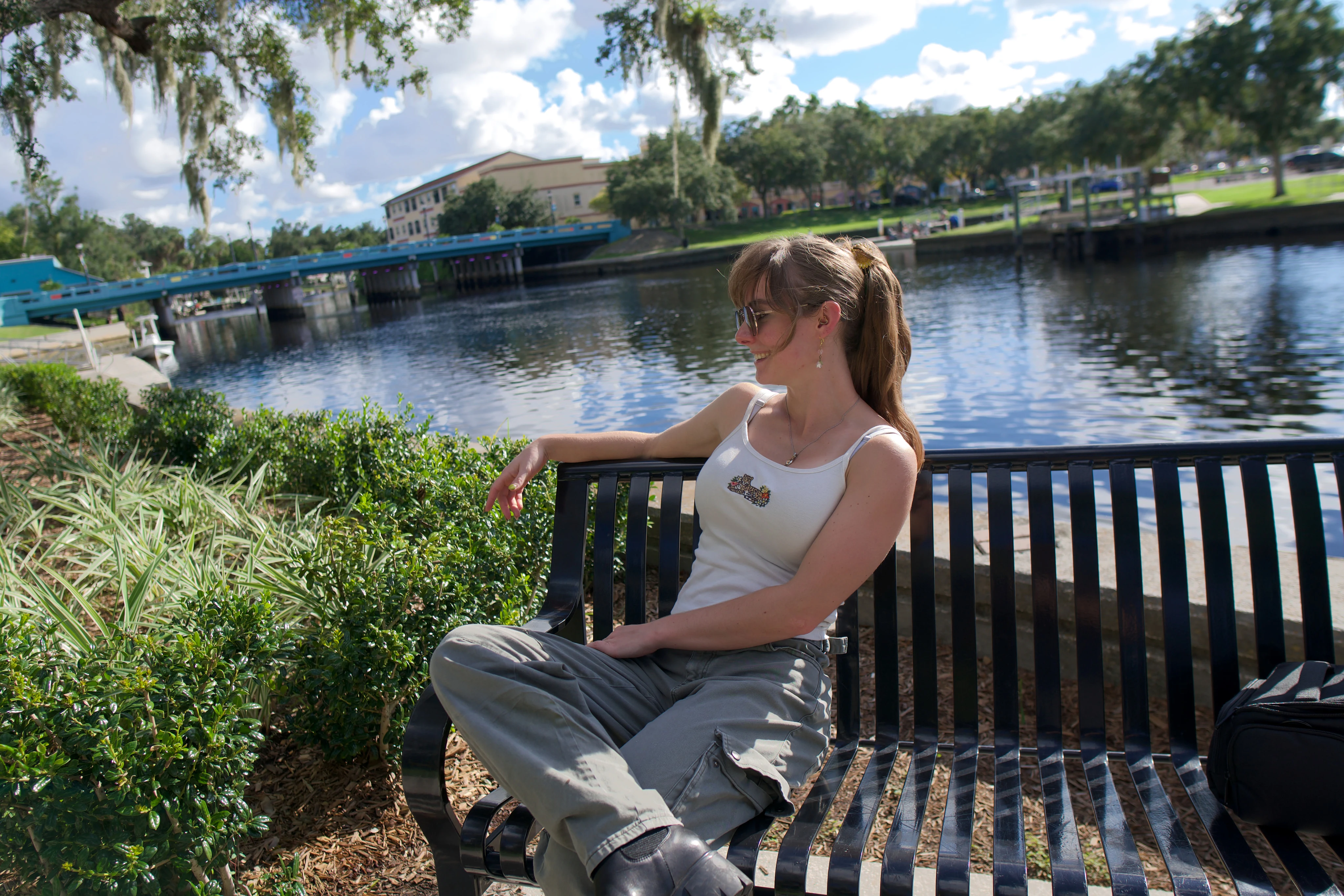 A woman on a black metal bench by the water, looking down