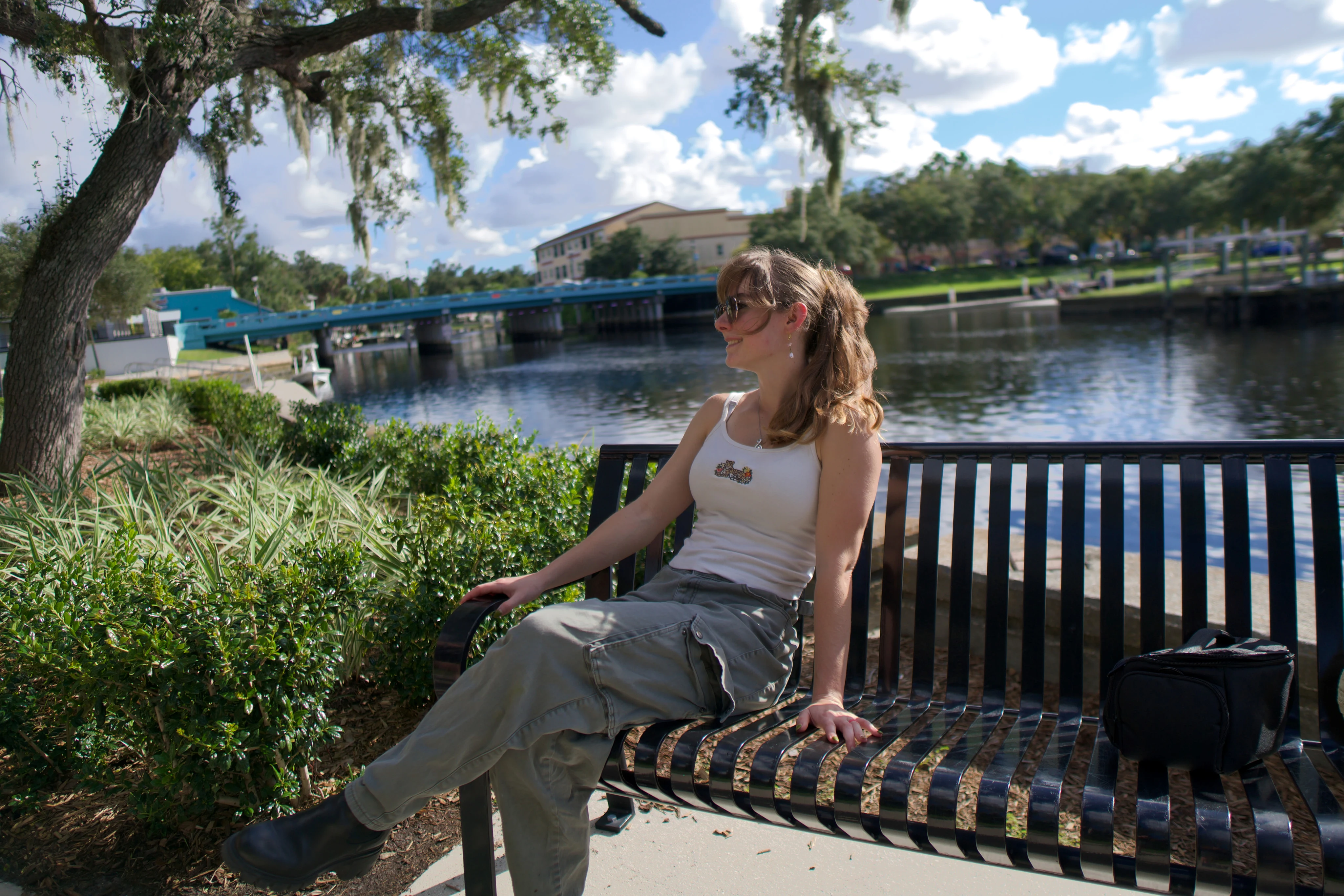 A woman on a waterside bench with one arm resting along the back
