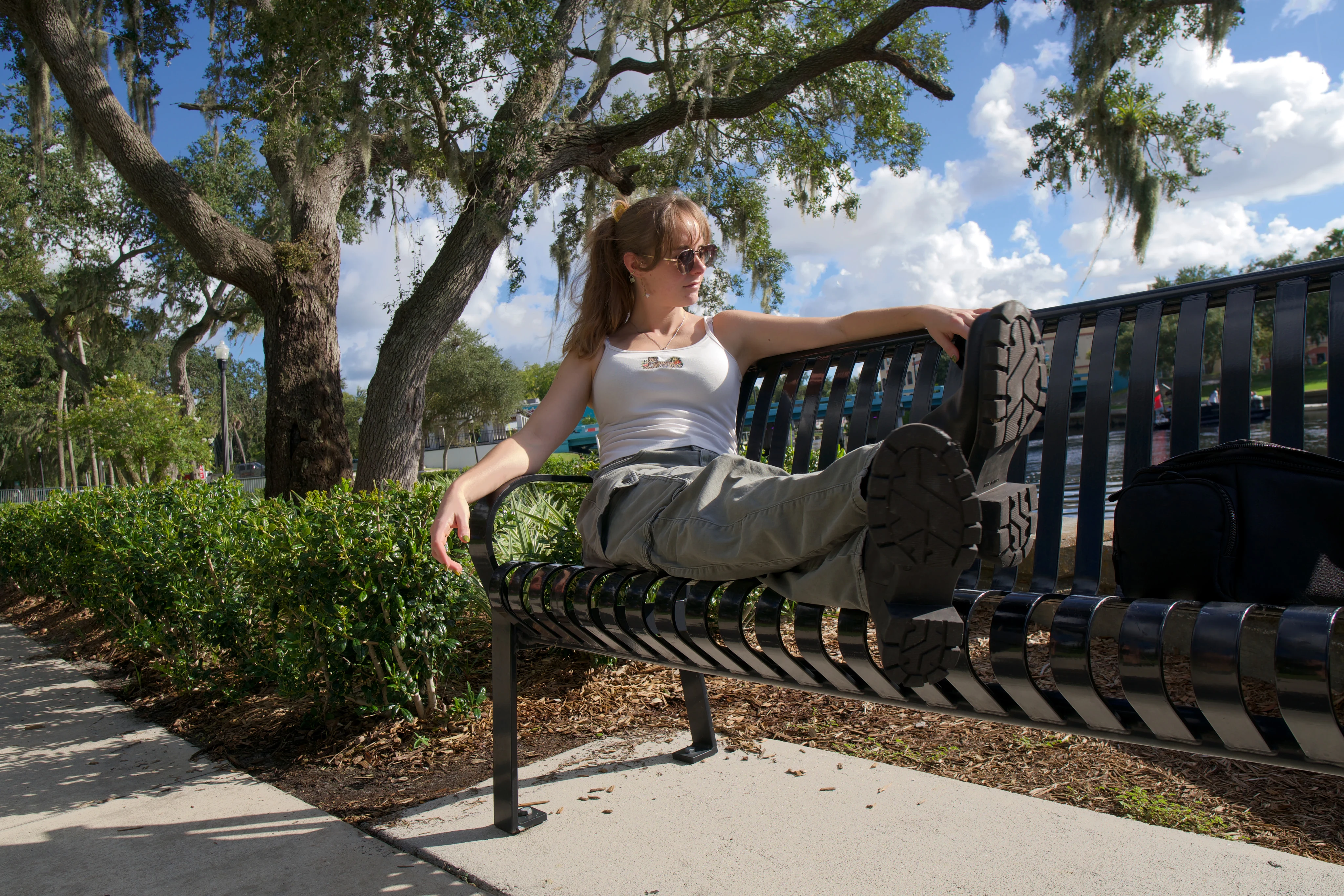 A woman lying across a metal bench with one boot up on the backrest