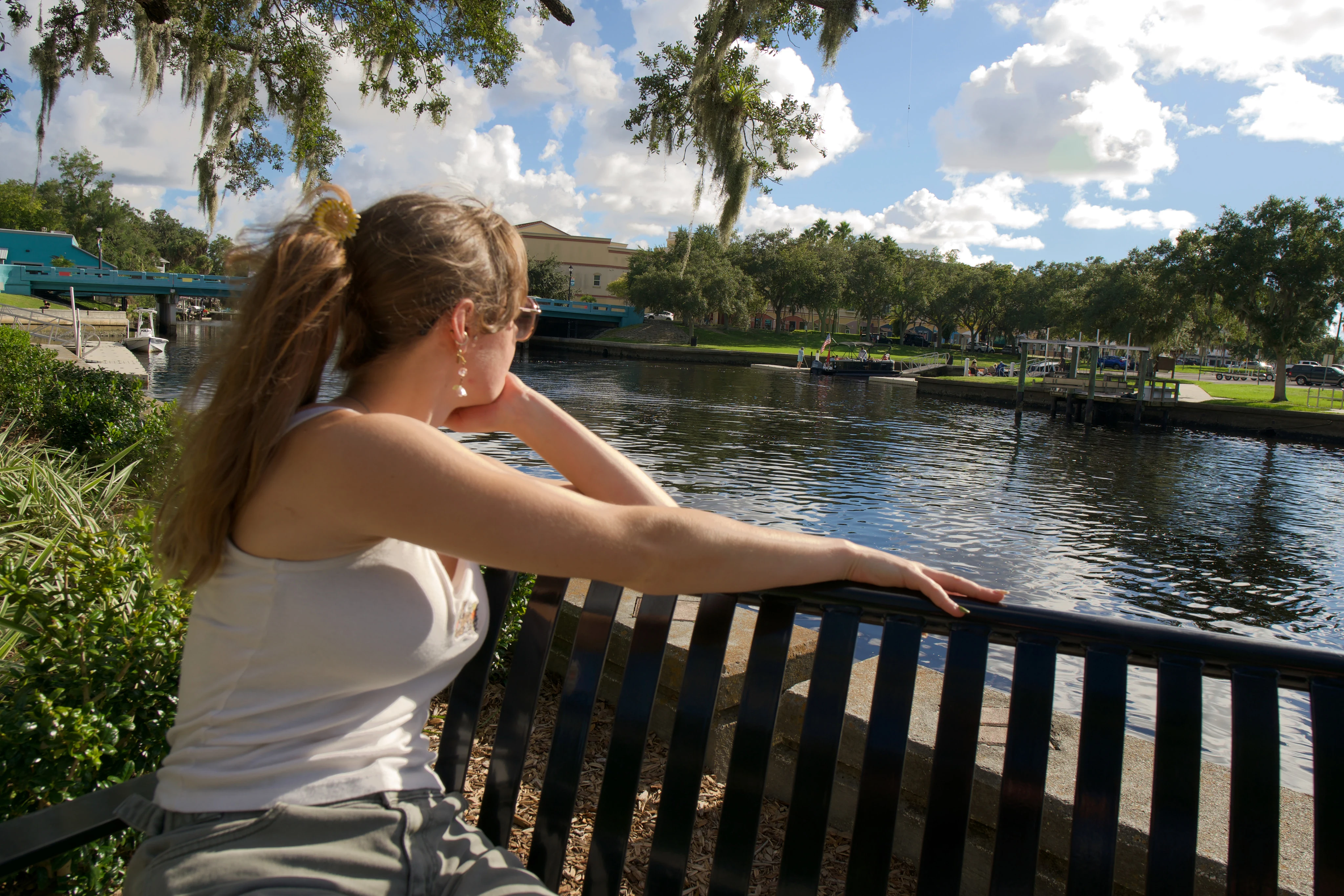 A woman seated on a bench from behind, arm along the rail, looking out over the water